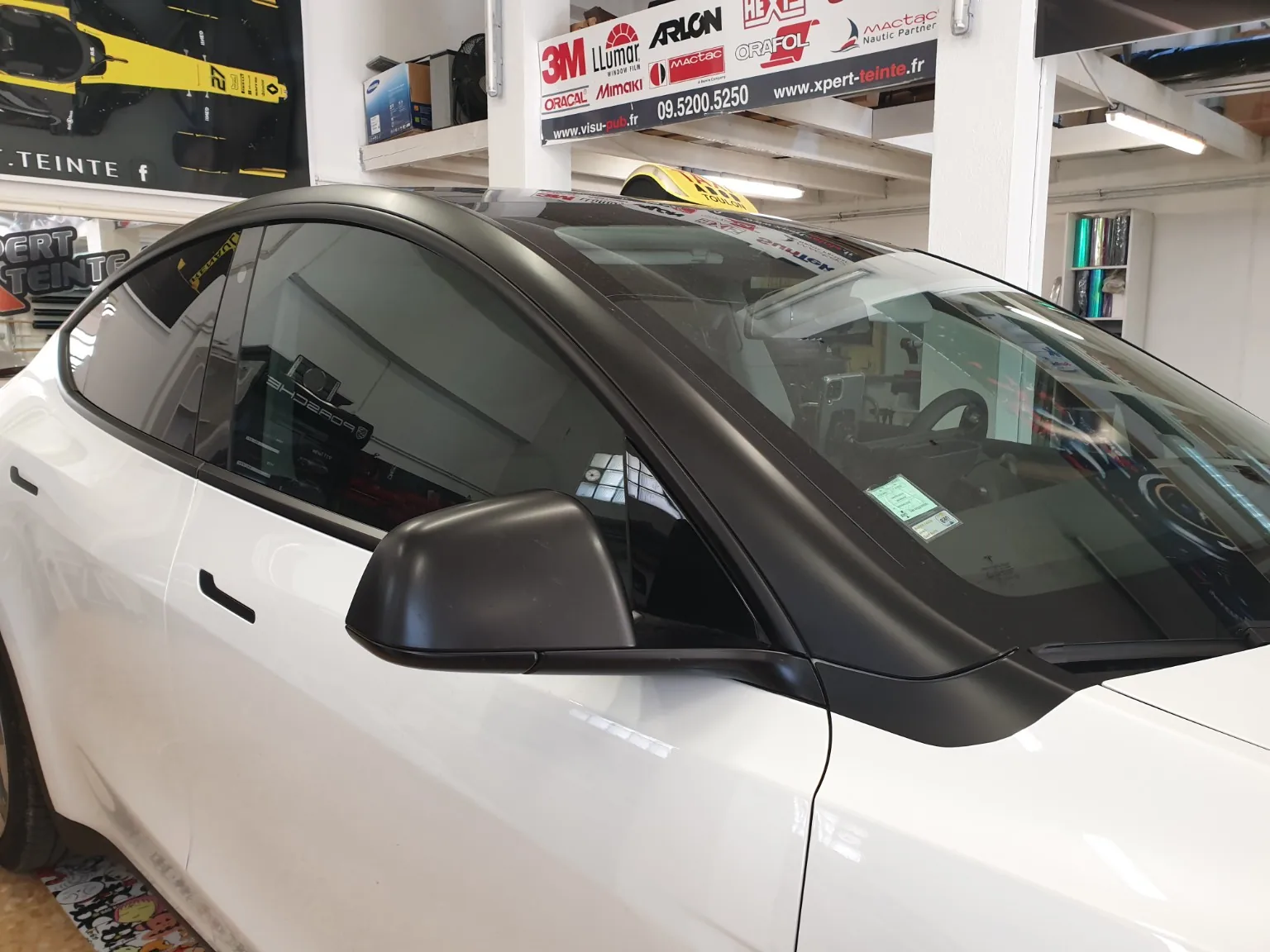 Tesla blanche vue de trois quarts avant, avec rétroviseur noir et vitrage latéral visibles, dans l’atelier Xpert Teinte.